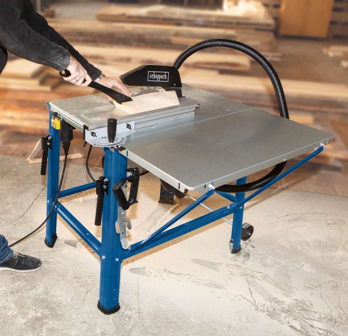 Tischkreissäge HS120o von Scheppach im Einsatz. Ein Benutzer führt ein Brett durch die Säge. Die Säge ist auf einem blauen Ständer montiert.