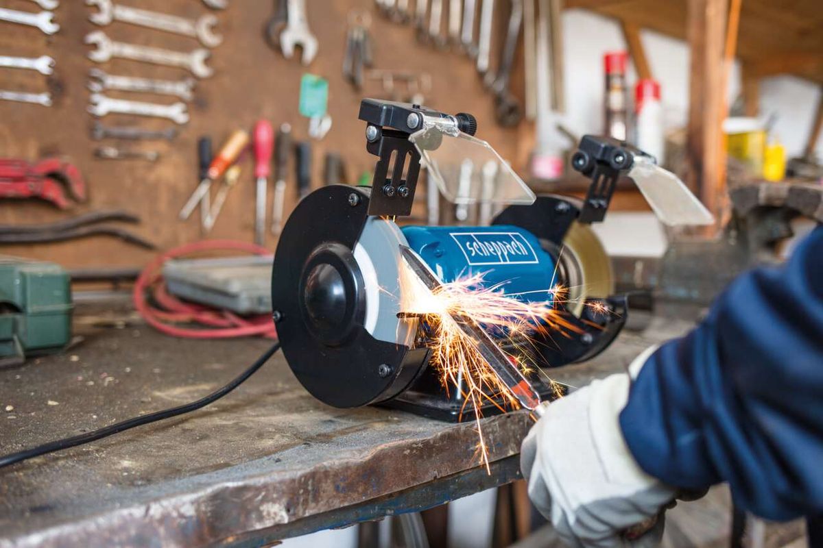 Ein Scheppach-Werkzeug wird in einer Werkstatt verwendet. Funken fliegen beim Arbeiten mit dem Gerät. Im Hintergrund hängen verschiedene Werkzeuge an der Wand.