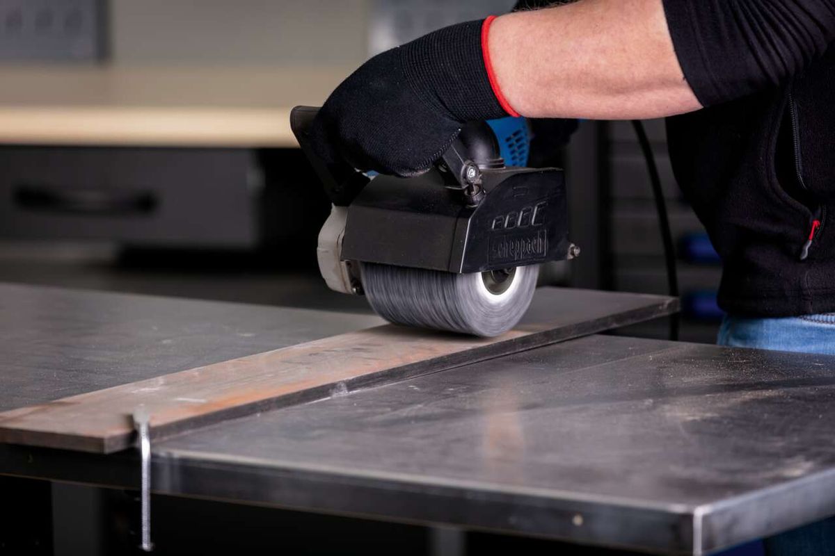 Scheppach Siliziumkarbidbürste im Einsatz an einer MRS1300 Satiniermaschine. Die Bürste wird von einem Nutzer geführt und bearbeitet eine Metallplatte.