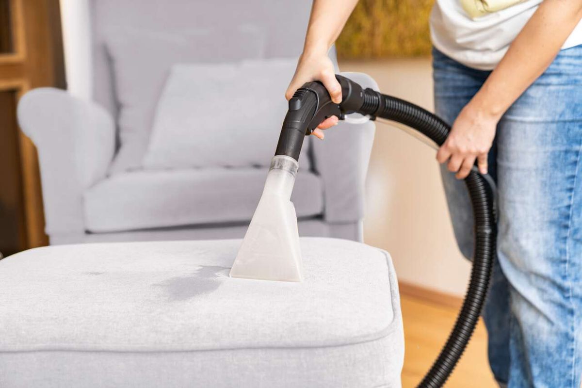 Ein Mensch reinigt mit dem Scheppach SprayVac20 einen hellgrauen Sessel. Der Sauger ist mit einem speziellen Aufsatz für Polstermöbel ausgestattet.