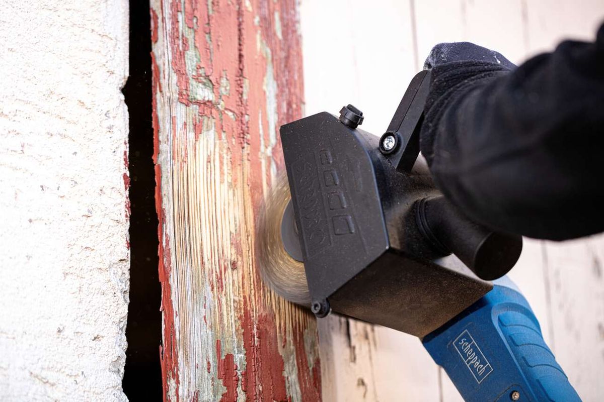 Scheppach Messingdrahtbürste im Einsatz an einer Maschine. Die Bürste wird von einer Person mit Handschuhen gehalten und bearbeitet eine rote, abgenutzte Oberfläche.