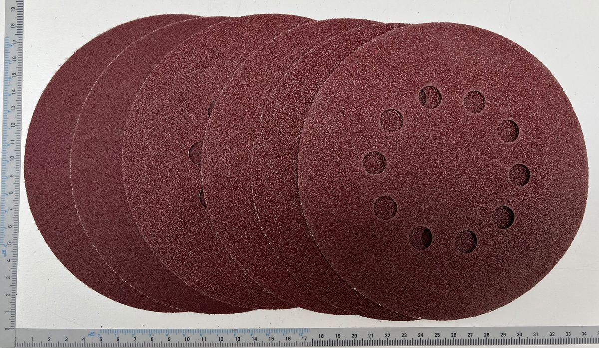 Ein Stapel aus zehn runden Schleifpapieren mit verschiedenen Körnungen, gemessen an einem Lineal. Die Scheiben haben Löcher für eine Schleifmaschine.