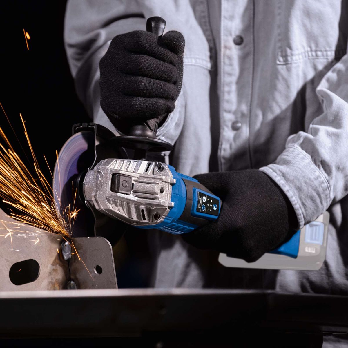 Werkzeug mit Akku-Winkelschleifer, Schutzhandschuh und Metallarbeitsstück mit Schleifspaß