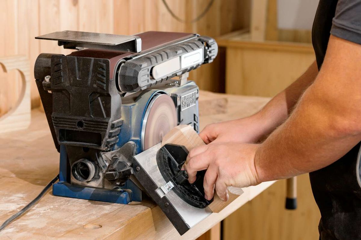 Band- und Tellerschleifer BTS900 Scheppach im Einsatz. Ein Nutzer schleift ein Holzstück mit dem Tellerschleifer. Die Maschine ist auf einem Holztisch platziert.