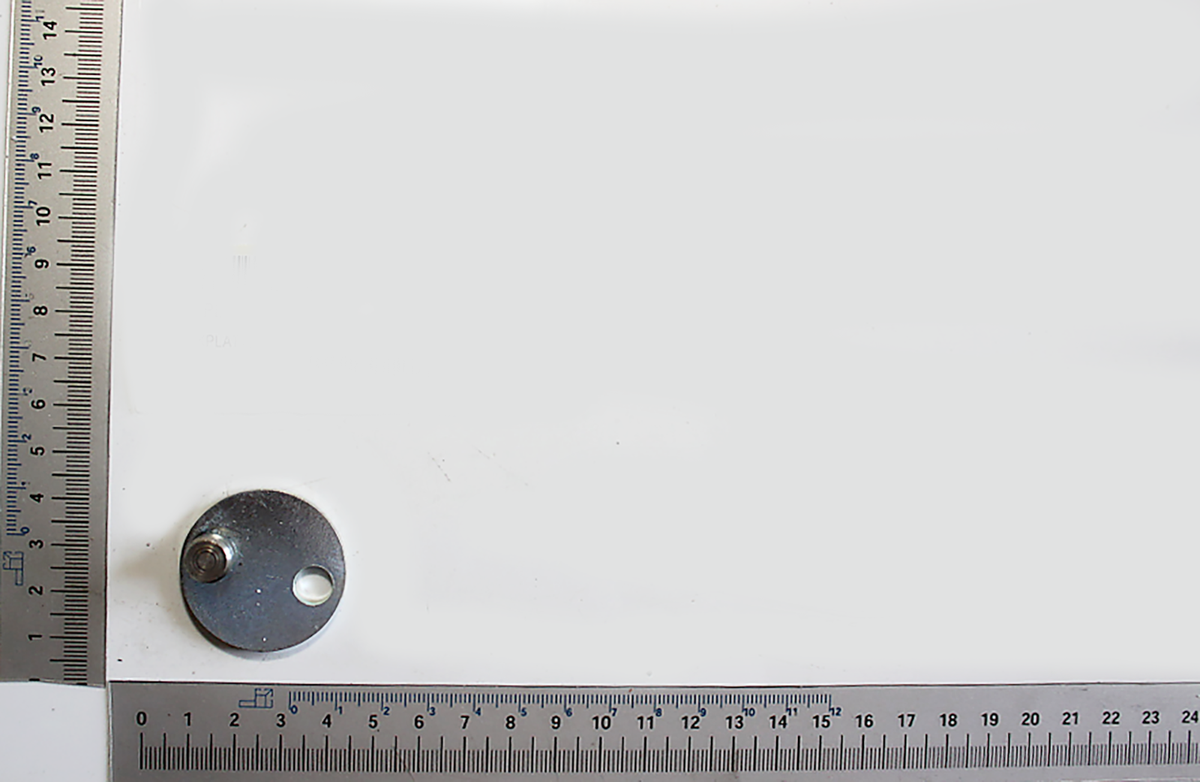 Metallplatte mit Loch und Gewinde, neben einer Messskala. Die Platte ist von der Seite zu sehen.