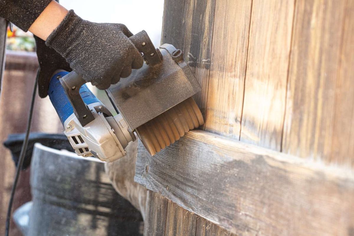 Scheppach Schleifstreifenbürste im Einsatz an der MRS1300 Satiniermaschine. Die Bürste wird von einer Hand in Arbeitshandschuhen gehalten und bearbeitet eine Holzoberfläche.