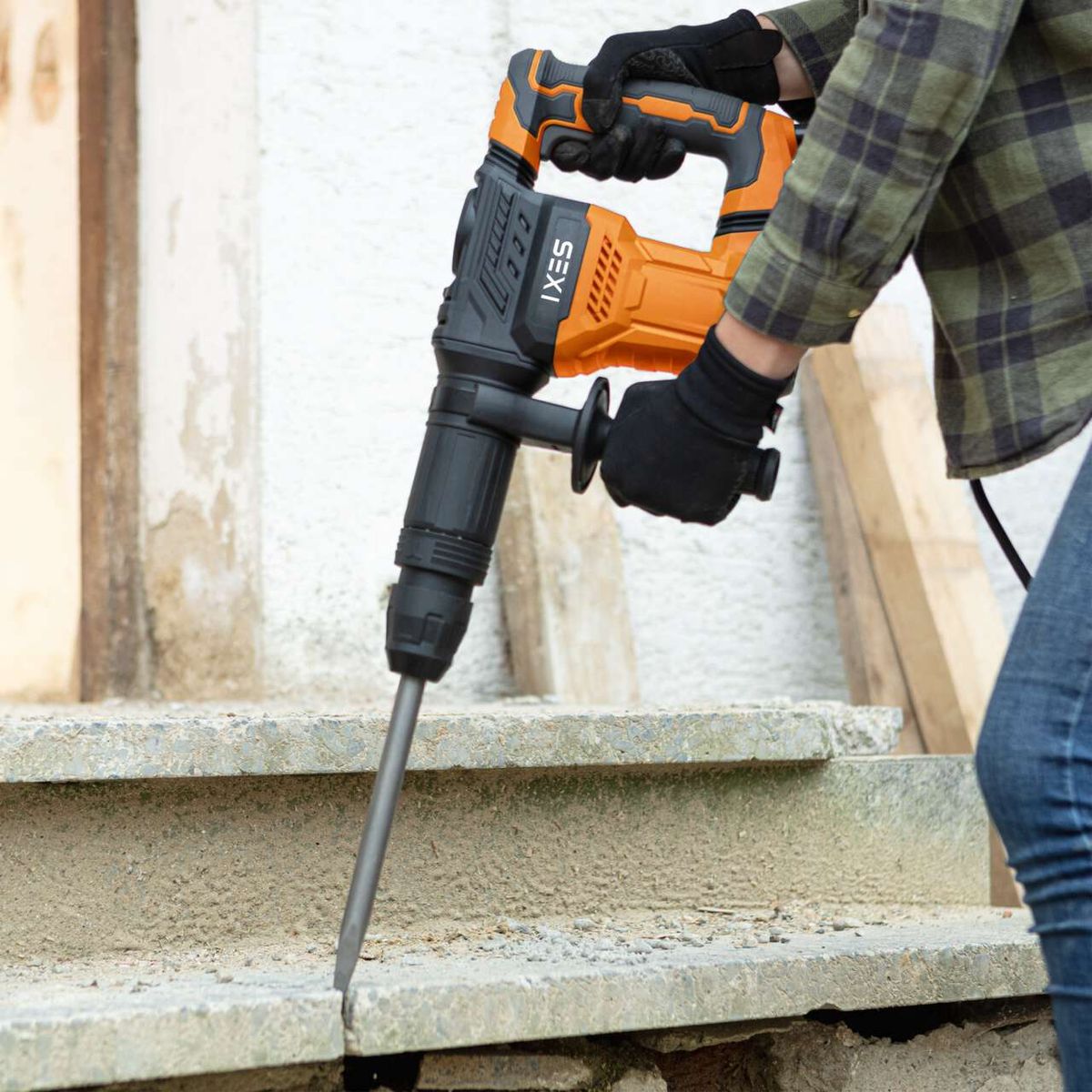 Der Scheppach Elektro-Abbruchhammer IX-DB1500 IXES mit orange-schwarzem Design und schwarzem Griff. Der Hammer wird von einem Arbeiter mit Handschuhen bedient und in eine Betonwand geschlagen.