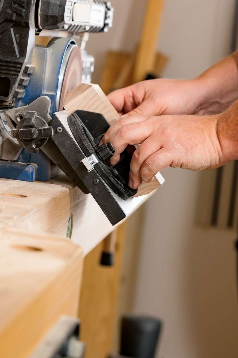 Ein Benutzer bedient den Scheppach Band- und Tellerschleifer BTS900, während er ein Holzstück schleift. Die Hände führen das Holz vorsichtig über die Schleifscheibe.