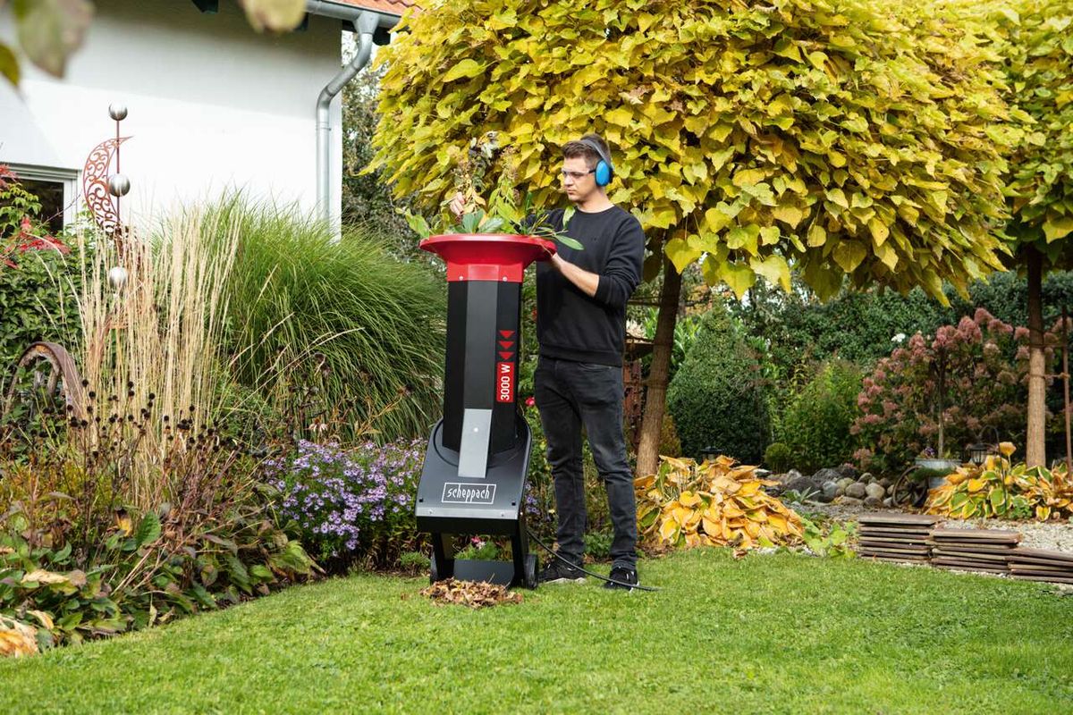 Mann betreibt Scheppach-Häcksler in einem Garten mit grünem Rasen und Pflanzen