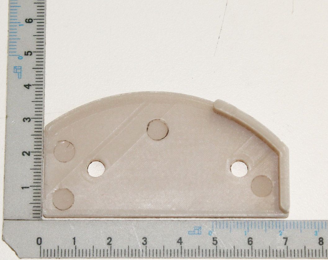 Nockenplatte aus Kunststoff mit vier Löchern, von oben fotografiert. Die Platte ist etwa 6 cm breit und 3 cm hoch.