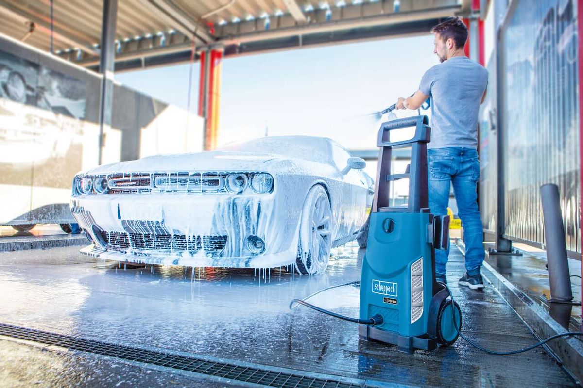 Ein Mann wäscht ein Auto mit dem Scheppach HCE2600 Elektro-Hochdruckreiniger. Der Hochdruckreiniger steht auf dem Boden und ist mit einem Schlauch verbunden.