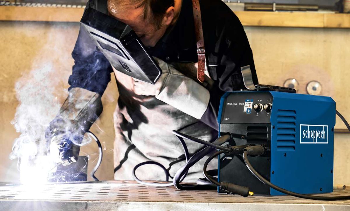 Ein Arbeiter schweißt mit dem Multischweißgerät WSE4000 von Scheppach. Der Schweißer trägt Schutzausrüstung und arbeitet an einem Metallstück. Der Schweißprozess erzeugt Rauch.