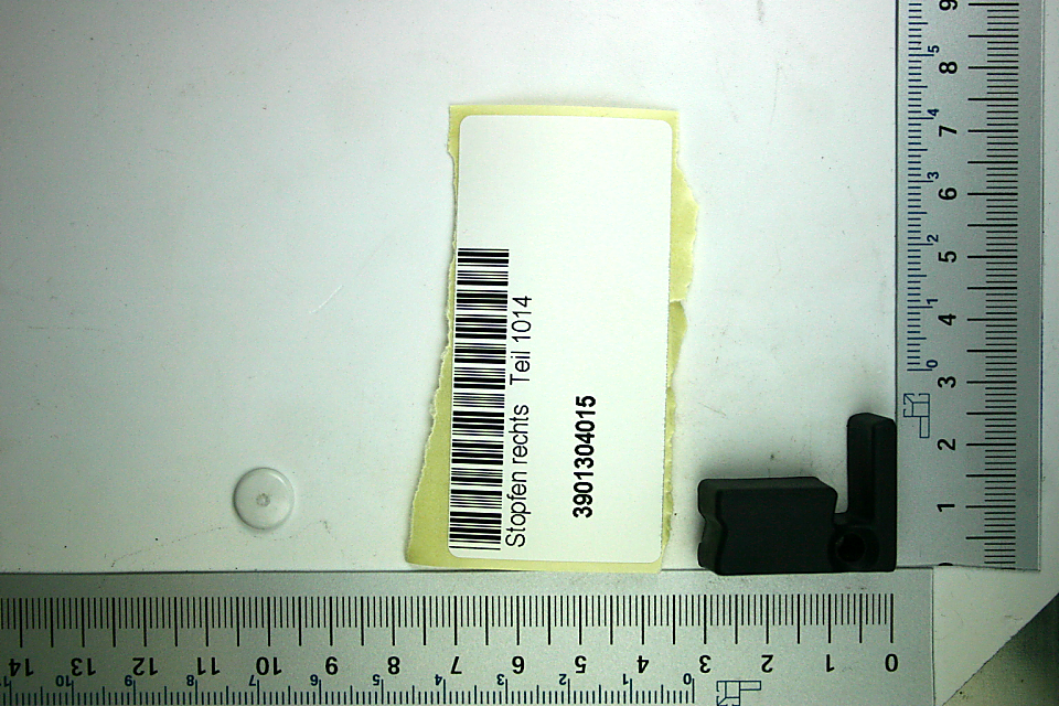 Ein schwarzes Kunststoffteil mit einem runden Loch und einem rechteckigen Ansatz. Dazu ein Aufkleber mit der Bezeichnung 'Stöpsen rechts Teil 1014' und der Artikelnummer 3901304015.