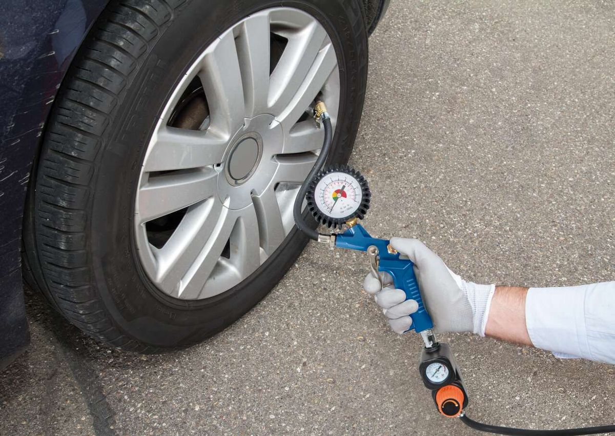 Ein Scheppach-Kompressor wird verwendet, um den Reifendruck eines Autos zu überprüfen. Der Kompressor ist mit einem Druckmesser ausgestattet und wird von einer Person mit Handschuhen bedient.