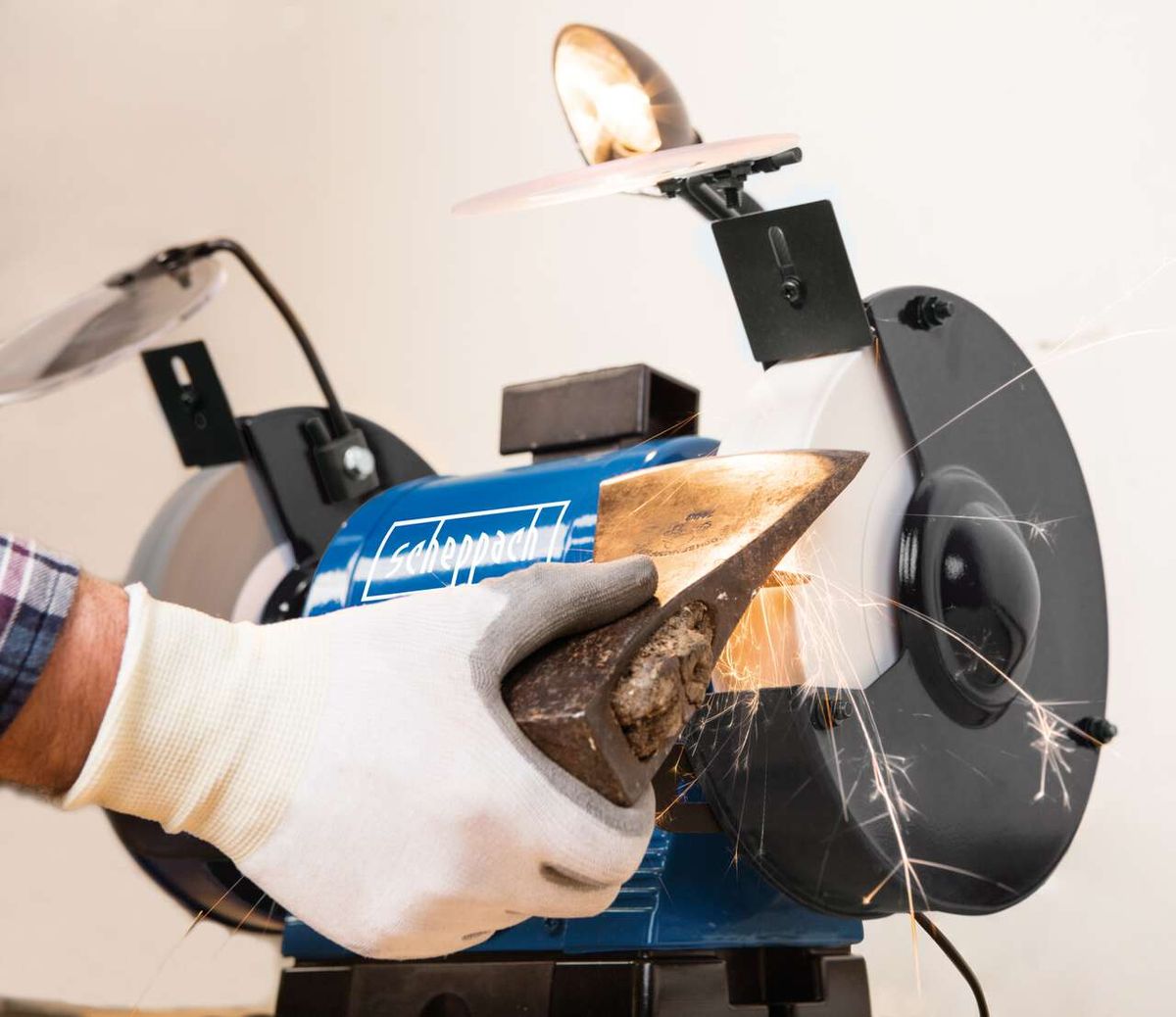 Scheppach Doppelschleifer BG200AL im Einsatz. Ein Handschuh hält ein Werkstück gegen die Schleifscheibe. Funken sprühen. Die Scheppach-Schriftzug ist auf dem Gehäuse sichtbar.