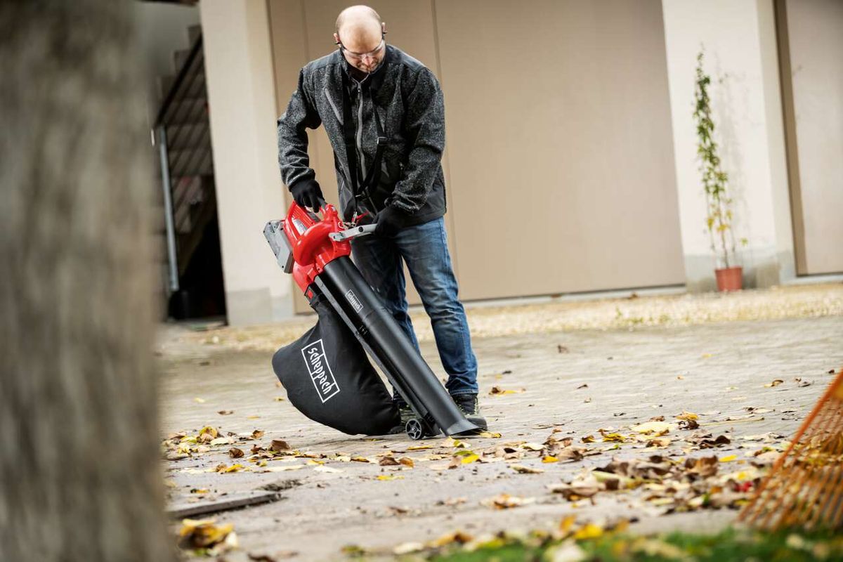 Ein Mann bedient den Laubsauger und -bläser BBV500-40Li von Scheppach auf einer Betonfläche mit Laub.