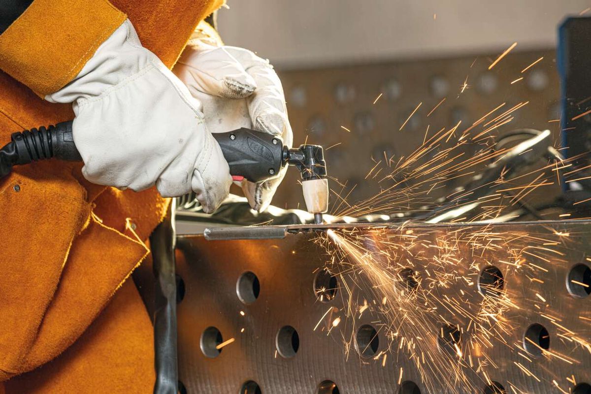 Ein Arbeiter verwendet das Scheppach 3in1 Kombi-Schweißgerät WSE4000-CUT zum Plasmaschneiden. Funken fliegen von der Schneidstelle weg. Der Arbeiter trägt Schutzhandschuhe und eine Schutzbrille.