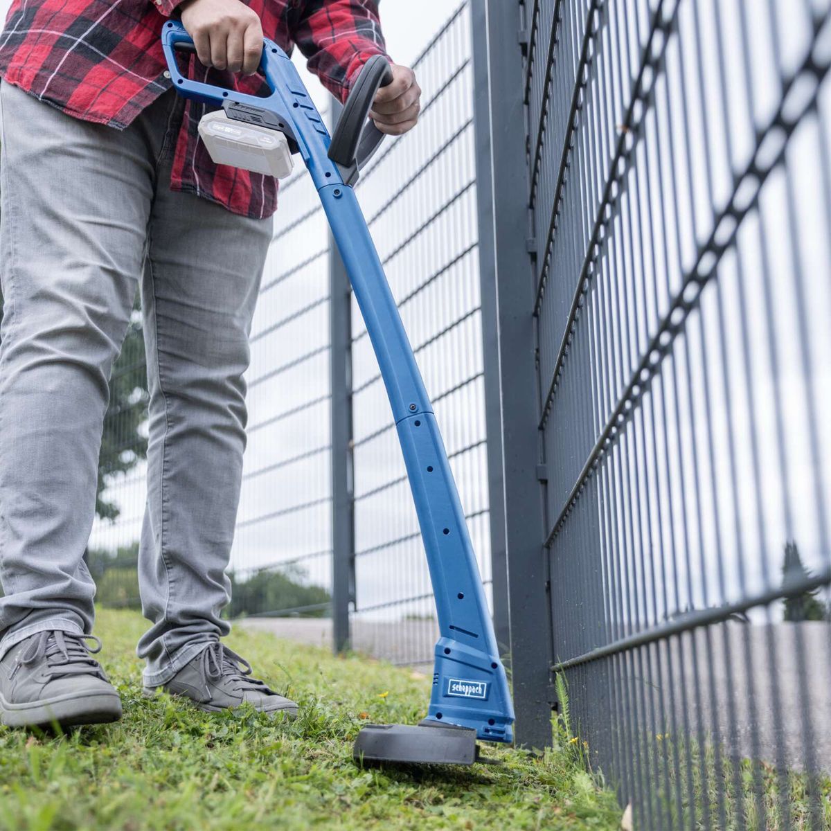 Person beim Einsatz eines Akku-Rasentrimmers mit Ladegerät und Ausleger für präzise Schnittarbeit