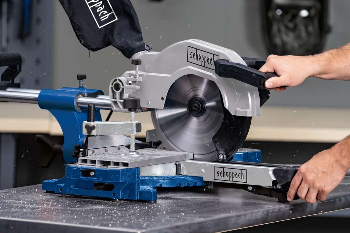 Kappzugsäge HM110MP von Scheppach im Einsatz. Die Säge schneidet ein Material, während ein Benutzer sie bedient. Die Säge ist auf einem blauen und silbernen Gestell montiert.