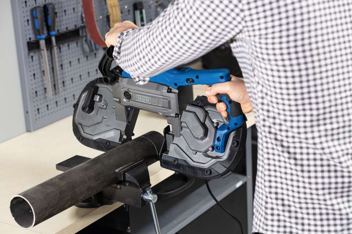 Metallbandsäge MBS1200xt von Scheppach im Einsatz. Eine Person bedient die Säge, die ein Metallrohr schneidet. Im Hintergrund sind Werkzeuge an der Wand befestigt.