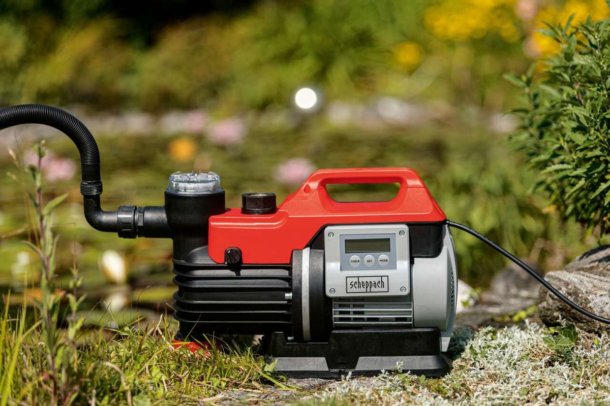 Hauswasserautomat GP1000 Jet LCD Scheppach, seitlich fotografiert. Im Hintergrund ist ein Garten mit Pflanzen zu sehen.