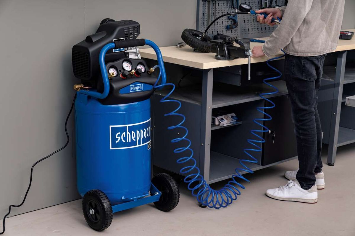 Scheppach Kompressor HC80V mit blauer Schlauchrolle und Werkbank. Ein Mann bedient den Kompressor.