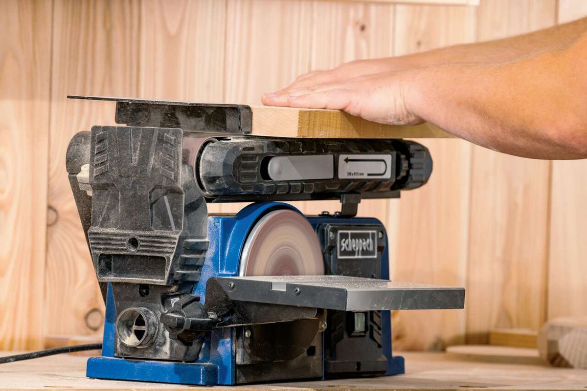 Band- und Tellerschleifer BTS900 von Scheppach. Ein Holzblock wird auf der Scheibe geschliffen. Die Maschine ist von der Seite zu sehen.