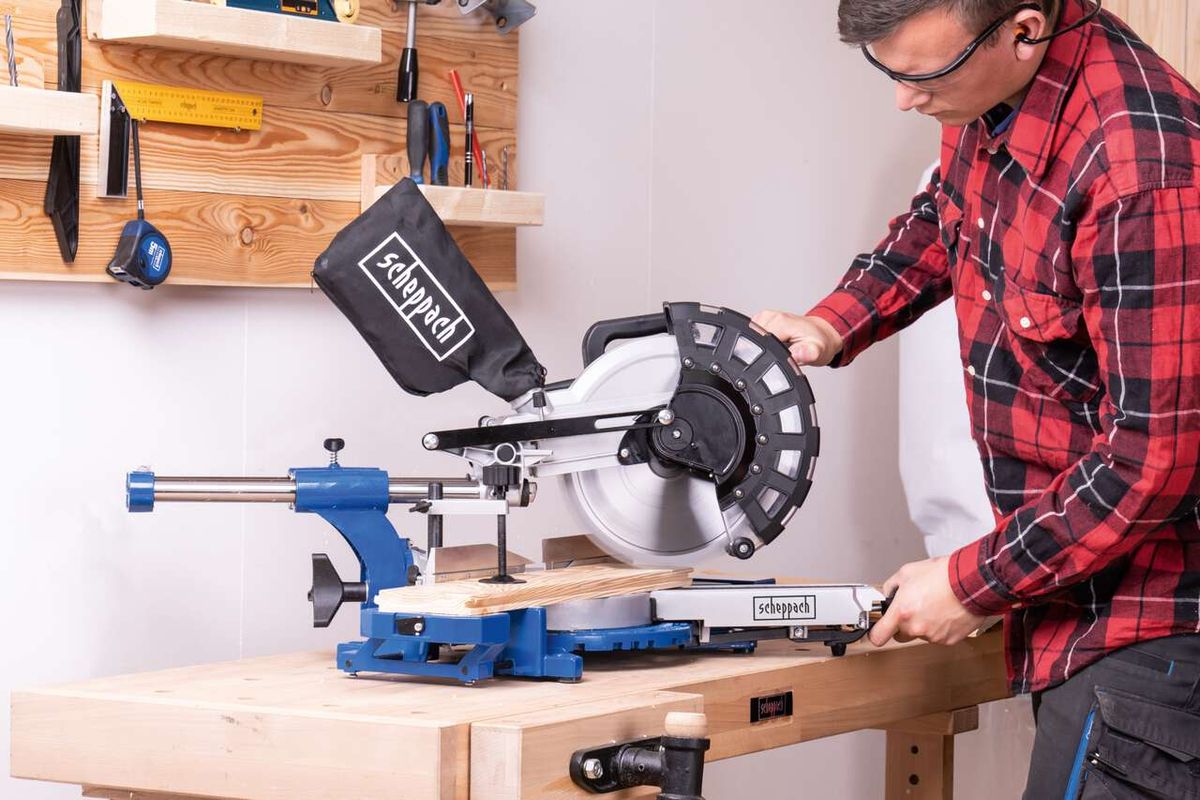 Scheppach-Kappzugsäge HM254 mit Sägeblatt, in Arbeitsumgebung mit Werkzeugaufhängung und Schutzbrille