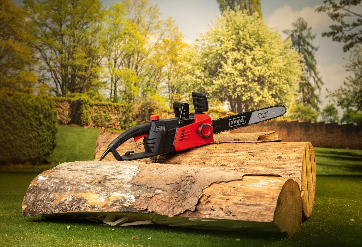 Elektro-Kettensäge CSE2700 von Scheppach auf einem Baumstamm im Garten. Die Säge liegt auf dem Holz und ist bereit für den Einsatz.