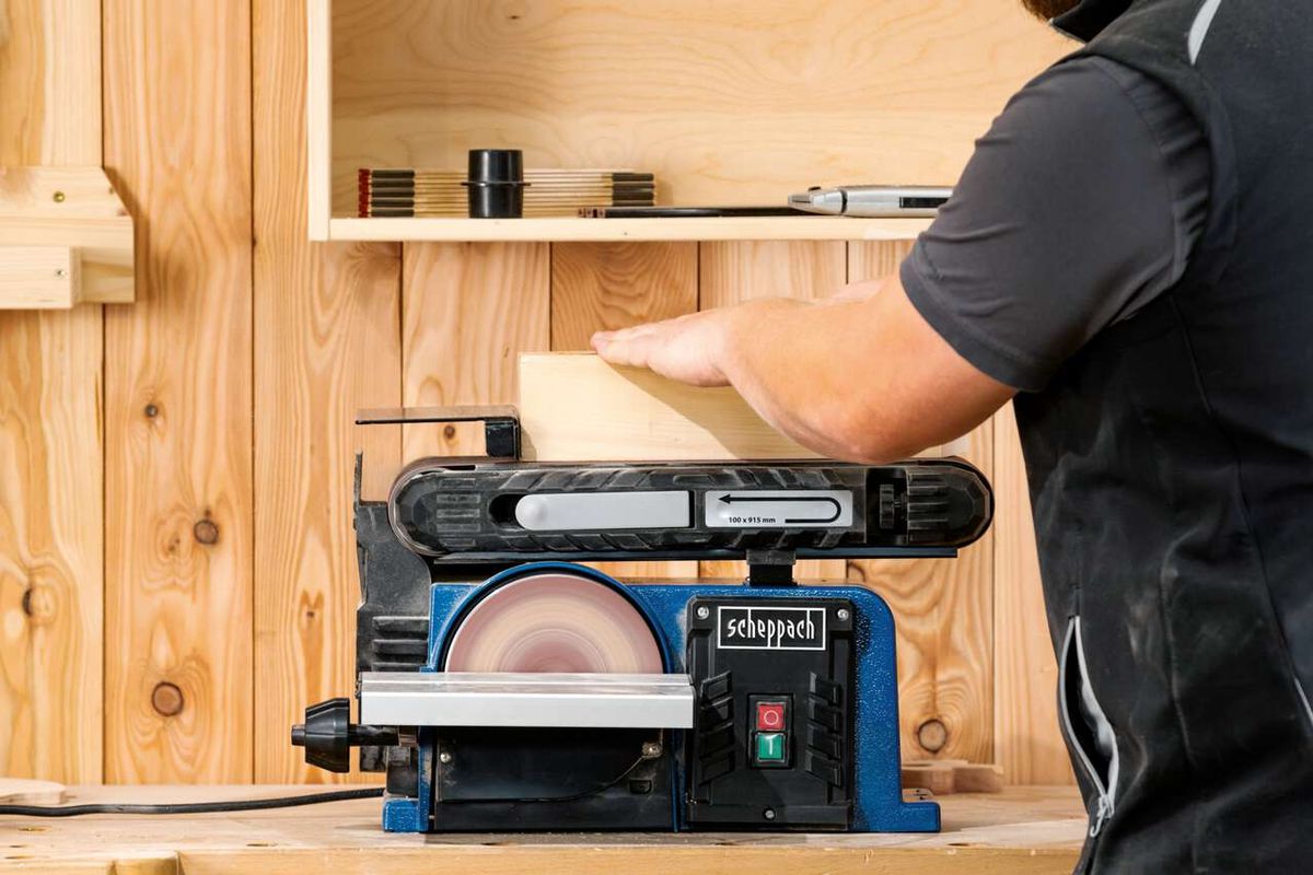 Band- und Tellerschleifer BTS900 von Scheppach im Einsatz. Ein Nutzer schleift ein Holzbrett. Der Schleifer hat eine 100 x 915 mm Schleifbandgröße und ist 370W stark.