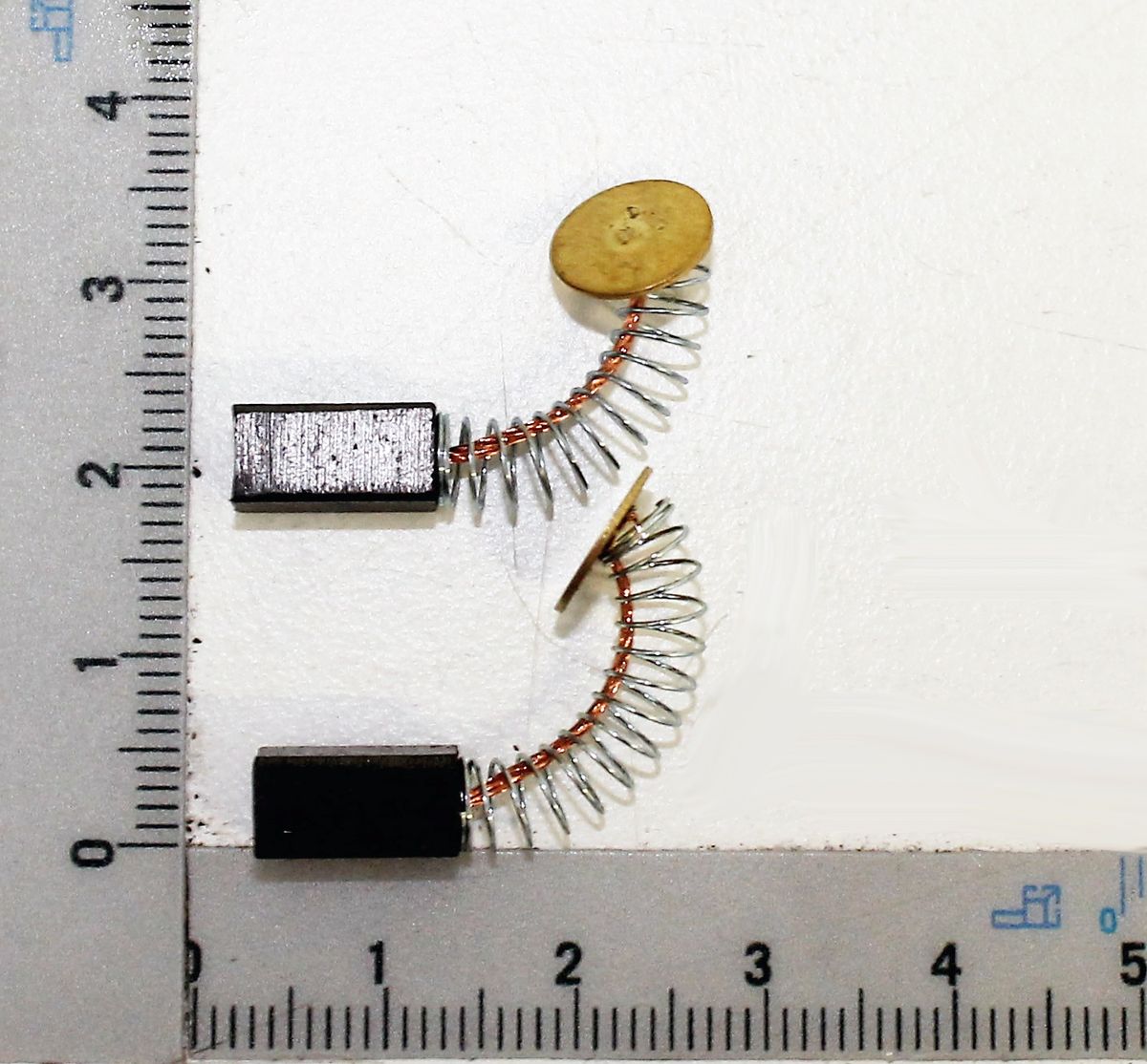 Kohlebürstensatz 5,3x5,3x10,5 (1 Satz = 2 Stück) auf einem Lineal. Die Kohlebürsten sind mit Spiralfedern verbunden.