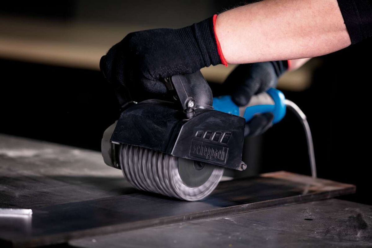 Gedrehte Metalldrahtbürste von Scheppach im Einsatz an einer Maschine. Die Bürste wird von einer Hand mit Schutzhandschuh gehalten.