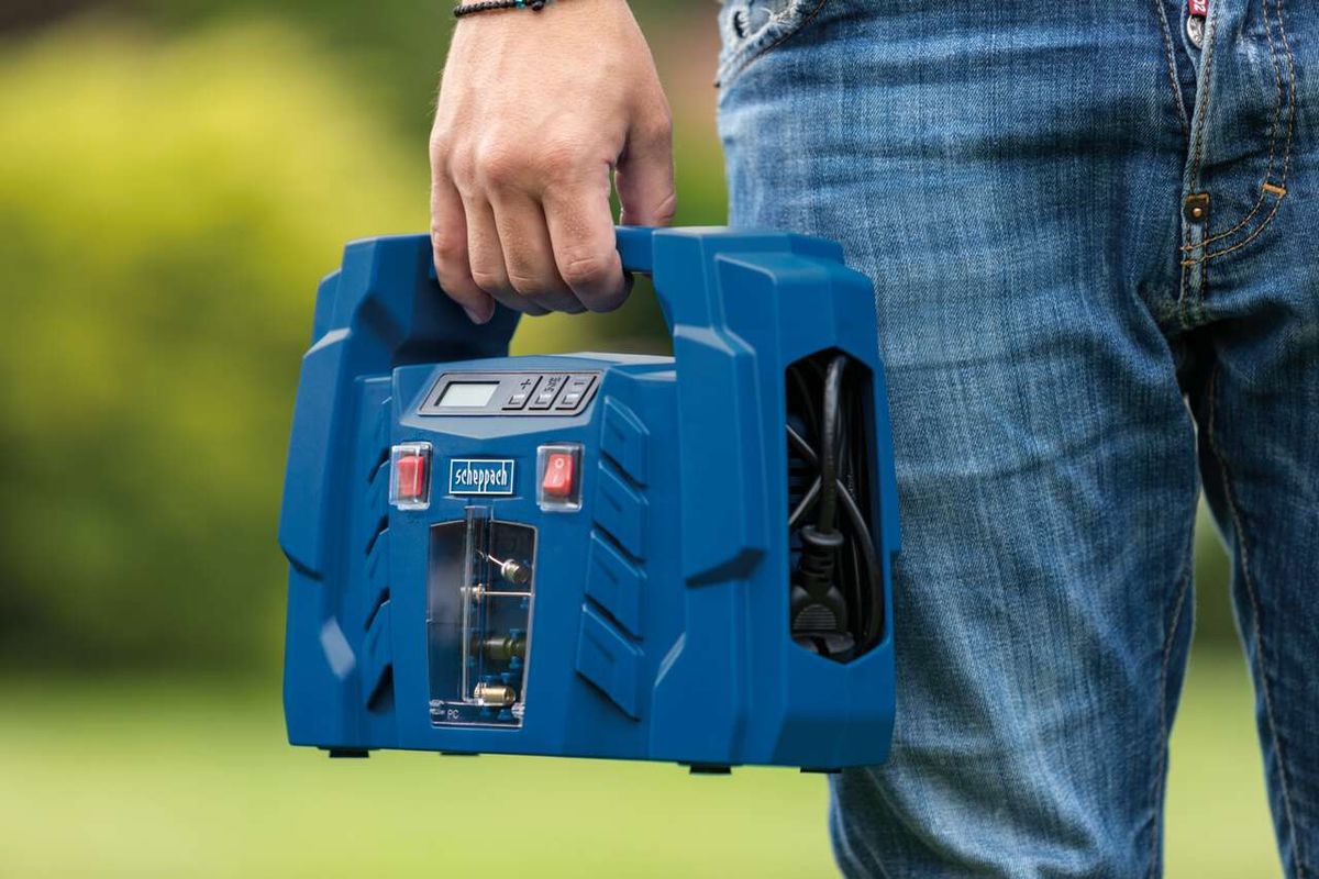 Ein Mann hält einen tragbaren Kompressor von Scheppach. Der Kompressor hat ein LCD-Display und verschiedene Anschlüsse.