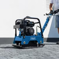 Ein Arbeiter bedient einen Scheppach-Baumaschinen-Vibrator auf einem gepflasterten Boden. Der Vibrator hat einen schwarzen Motor und wird für Bodenverdichtungsarbeiten verwendet.