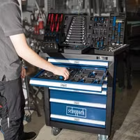 Ein Werkzeugwagen mit verschiedenen Werkzeugen und Zubehörteilen. Ein Mann greift nach einem Werkzeug im unteren Fach. Der Wagen hat mehrere Fächer und Schubladen für die Organisation der Werkzeuge.