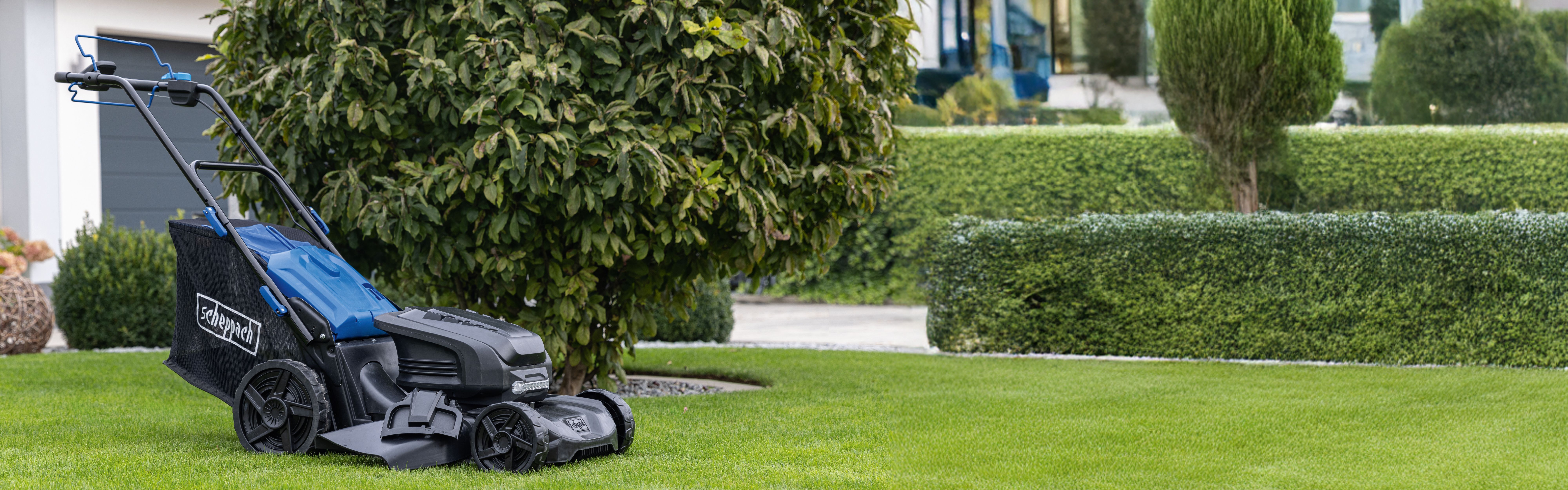 Scheppach-Gartenmäher auf grünem Rasen mit gepflegten Hecken und Bäumen im Hintergrund