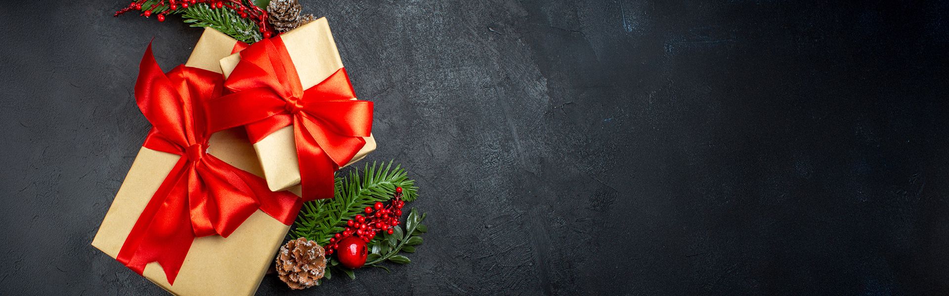 Gefüllte Geschenkboxen mit rotem Band und Weihnachtsdekoration wie Tannenzweige und Beeren