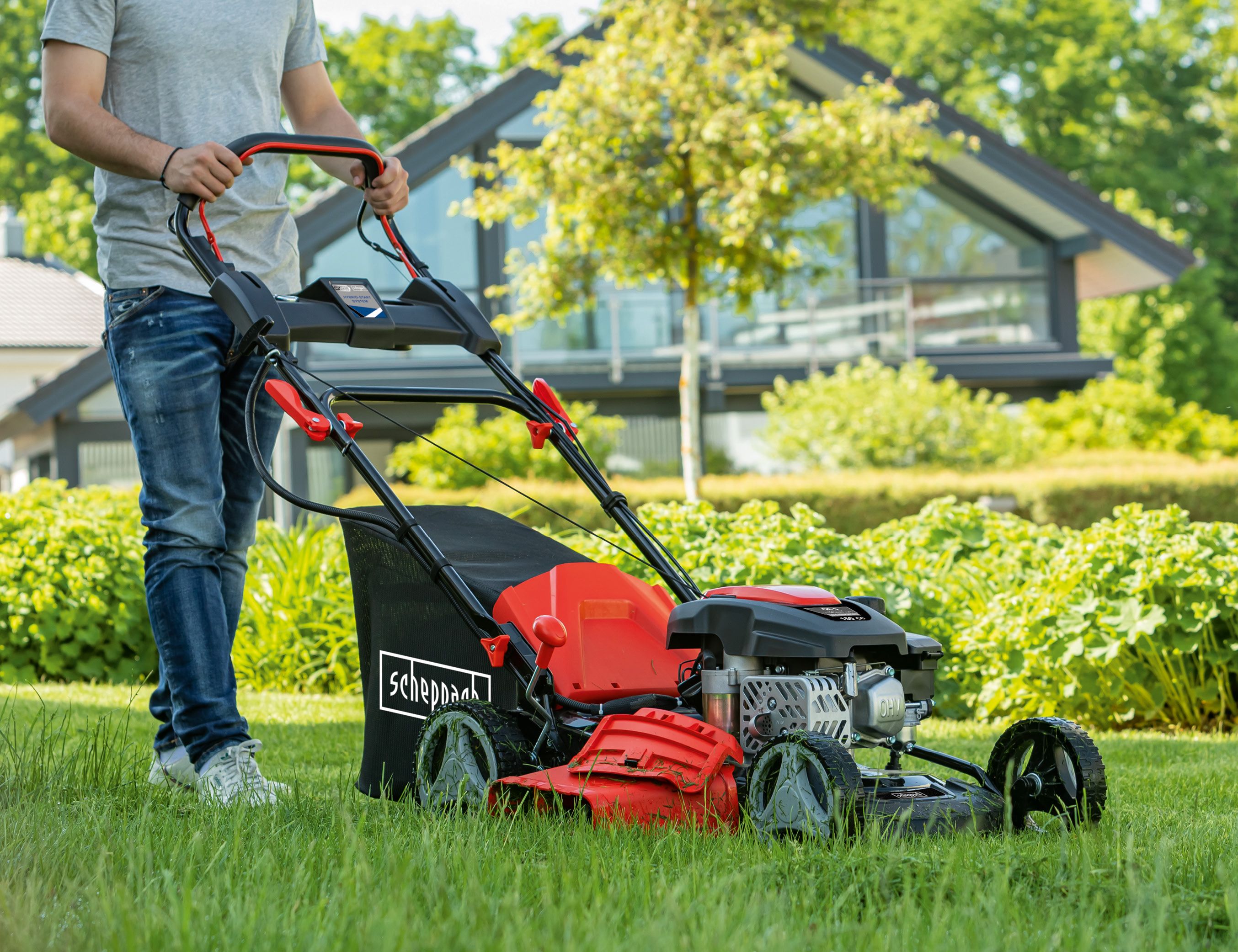 Mobiler Rasenmäher von Scheppach auf dem Gras mit Person, die ihn bedient