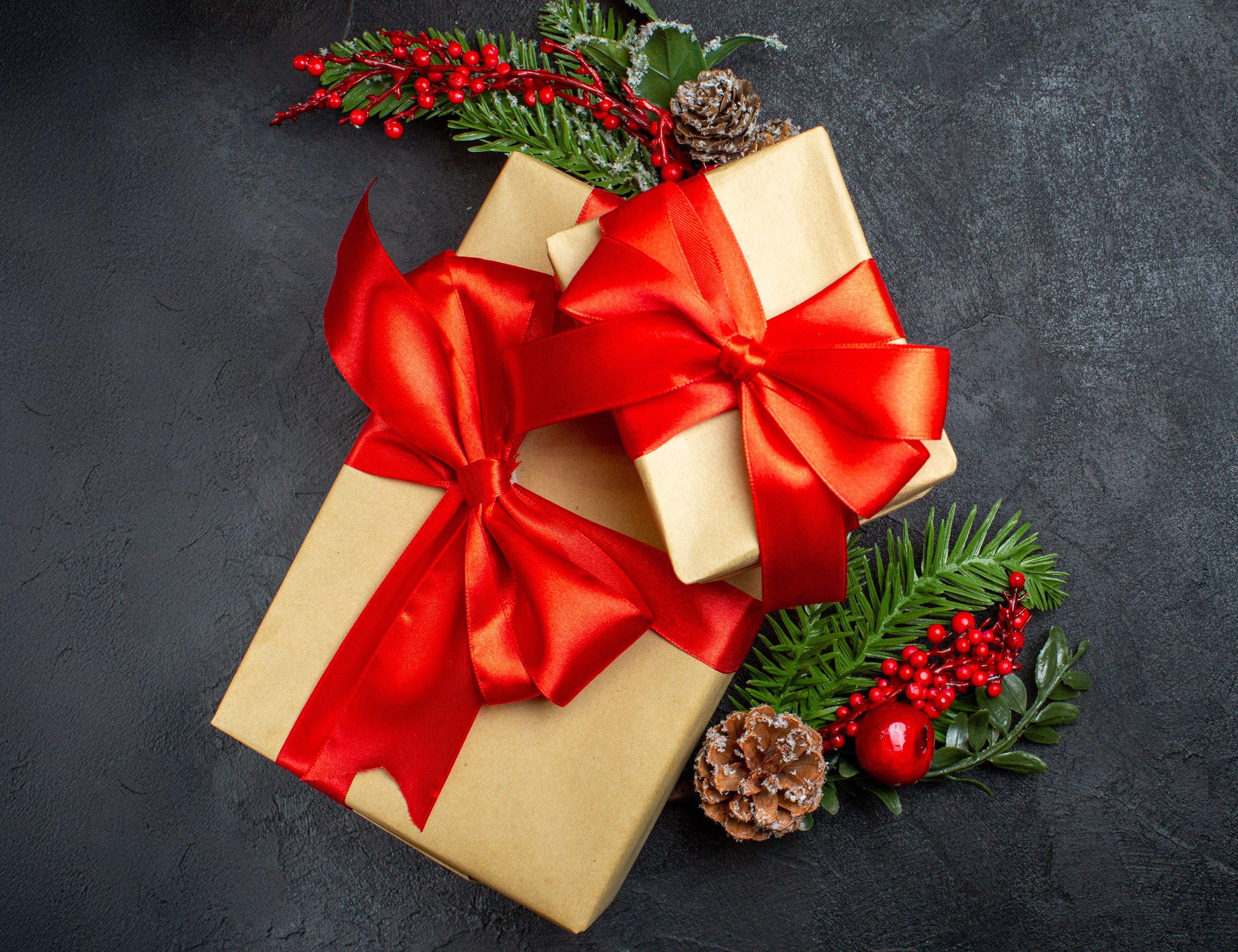 Gefüllte Geschenkboxen mit roten Band und Weihnachtsdekoration (grüne Tannenzweige, rote Beeren, Schneekugeln)