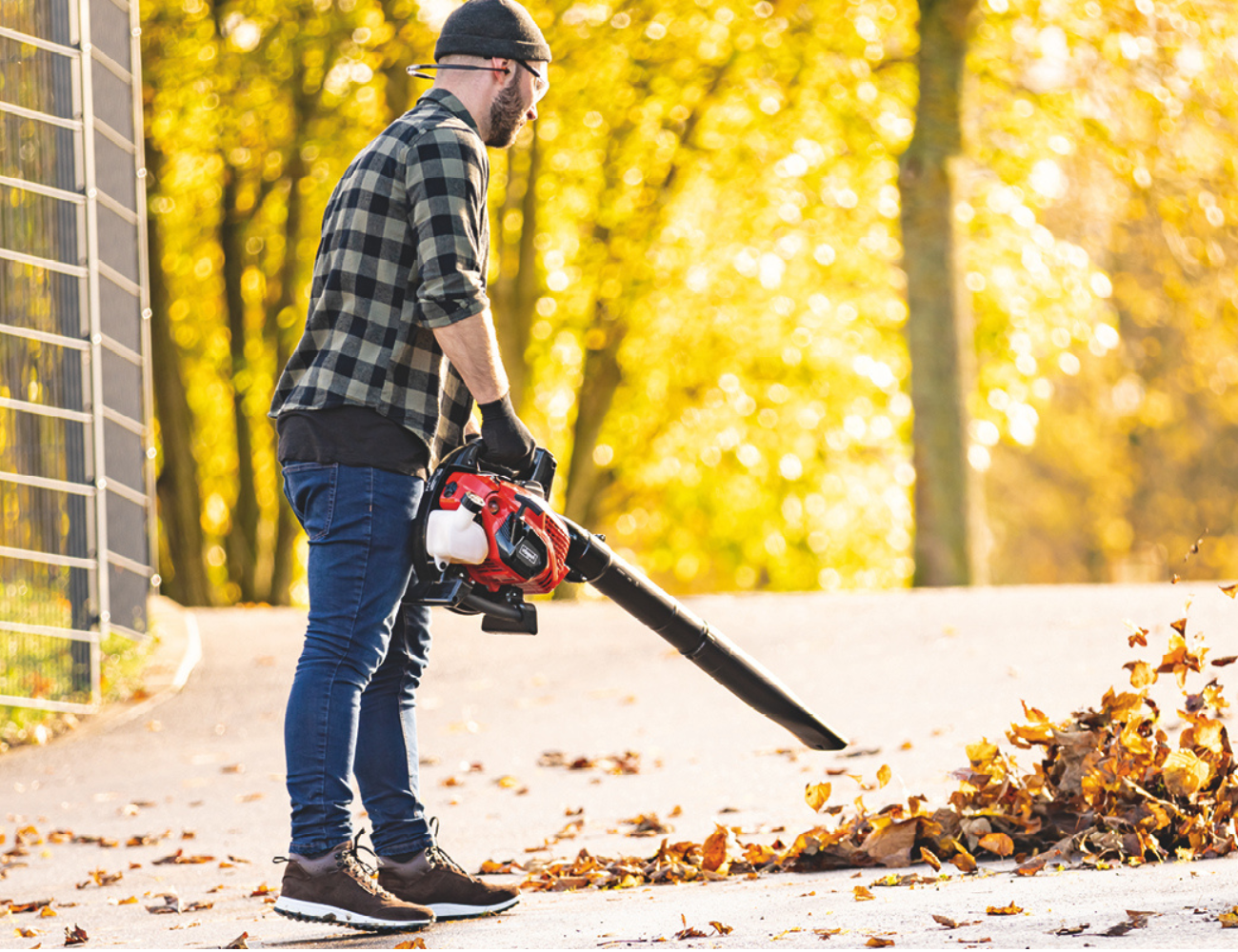 Ein Mann verwendet einen Laubsauger auf einem Weg mit herabgefallenen Blättern. Der Laubsauger ist ein Scheppach-Produkt.